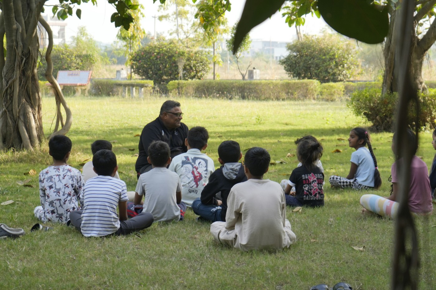 Grupo de niños y un instructor en círculo bajo un árbol durante una sesión al aire libre